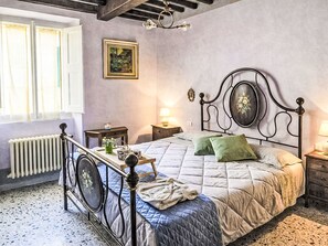 A bedroom with a bed, a radiator, a window with curtains, a bedside table with a lamp, and a wall-mounted picture. - Casa Beppina Cortona by Interhome (Cortona)