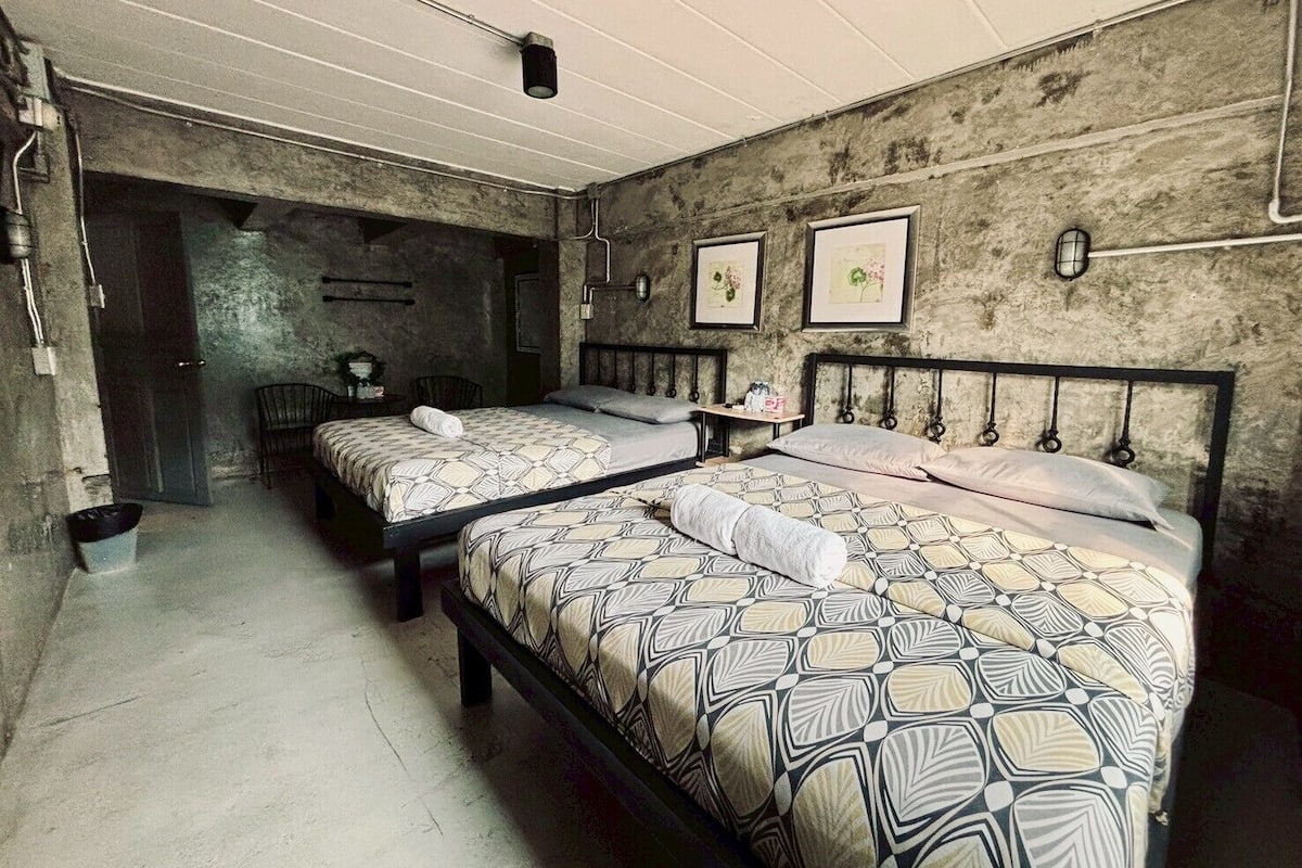 Une chambre avec deux lits, une petite table, une chaise et un luminaire fixé au mur.