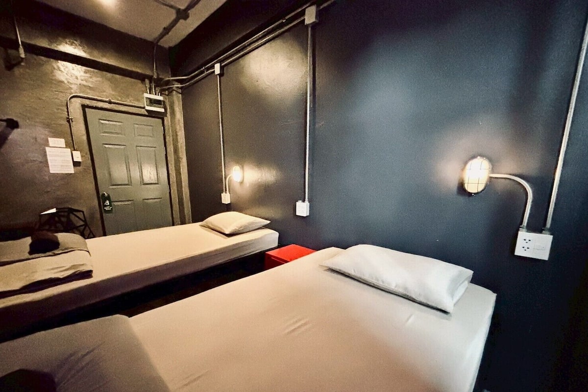 Une chambre d’hôtel avec un lit simple, une petite table, une chaise, un bureau et une porte.