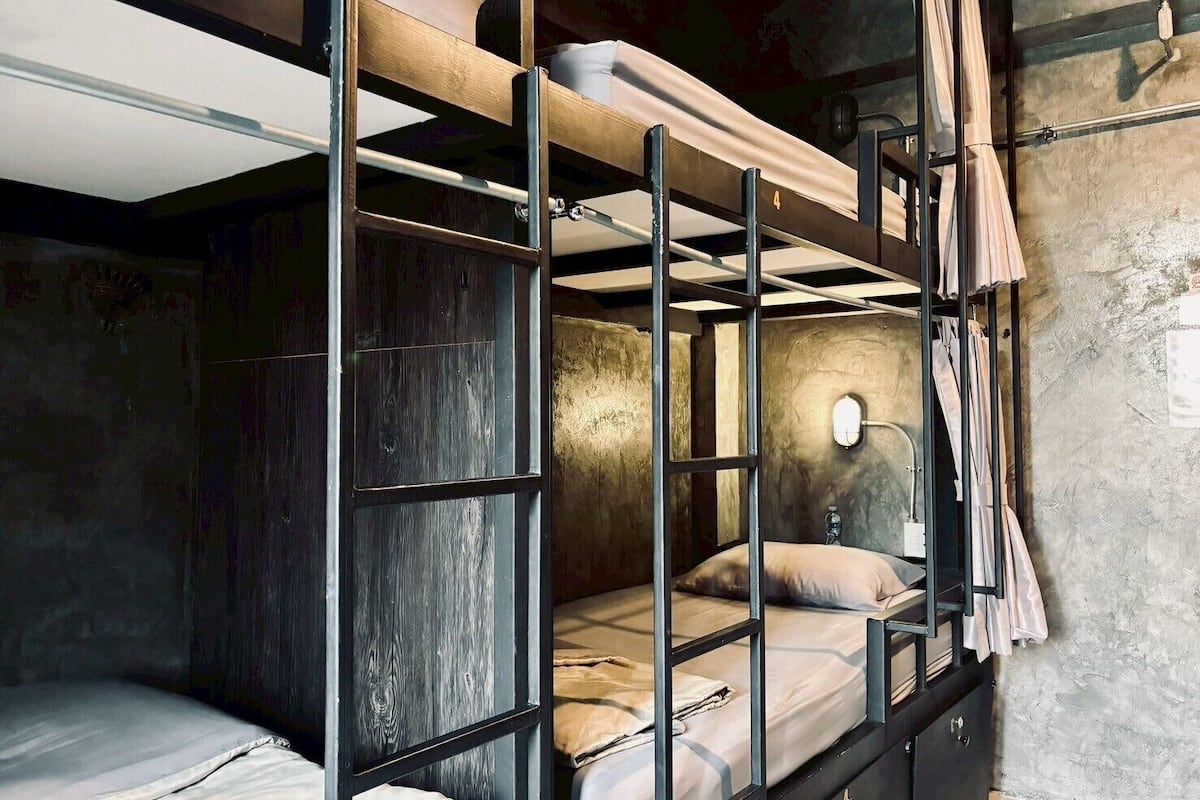 Un lit superposé avec une tête de lit, une table de chevet et un luminaire fixé au mur.