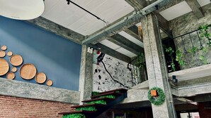 Un interior moderno con vigas de hormigón a la vista, una pared de ladrillo y una escalera con plantas verdes.