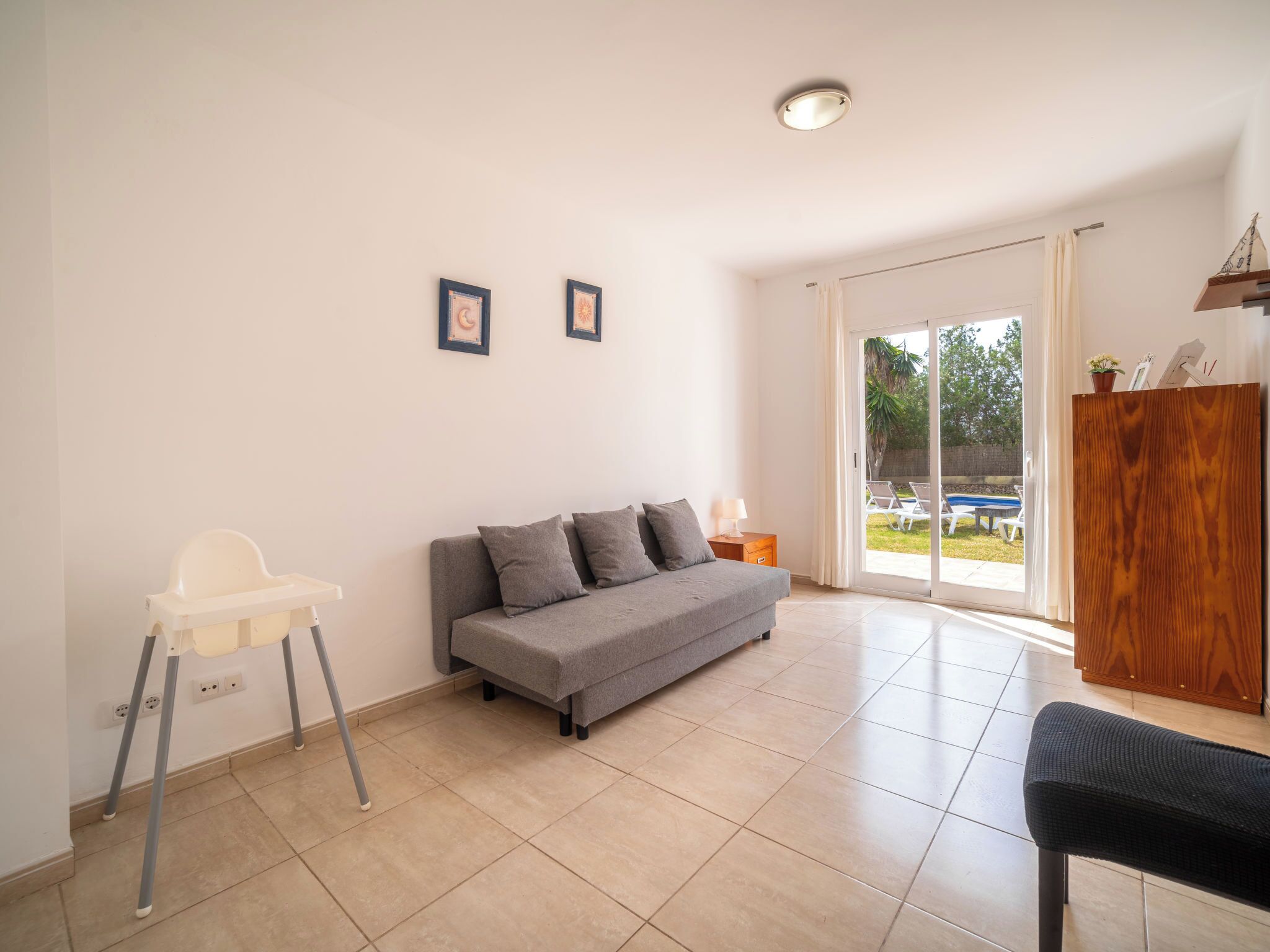 A spacious living area with a grey sofa, a white high chair, and a wooden cabinet.