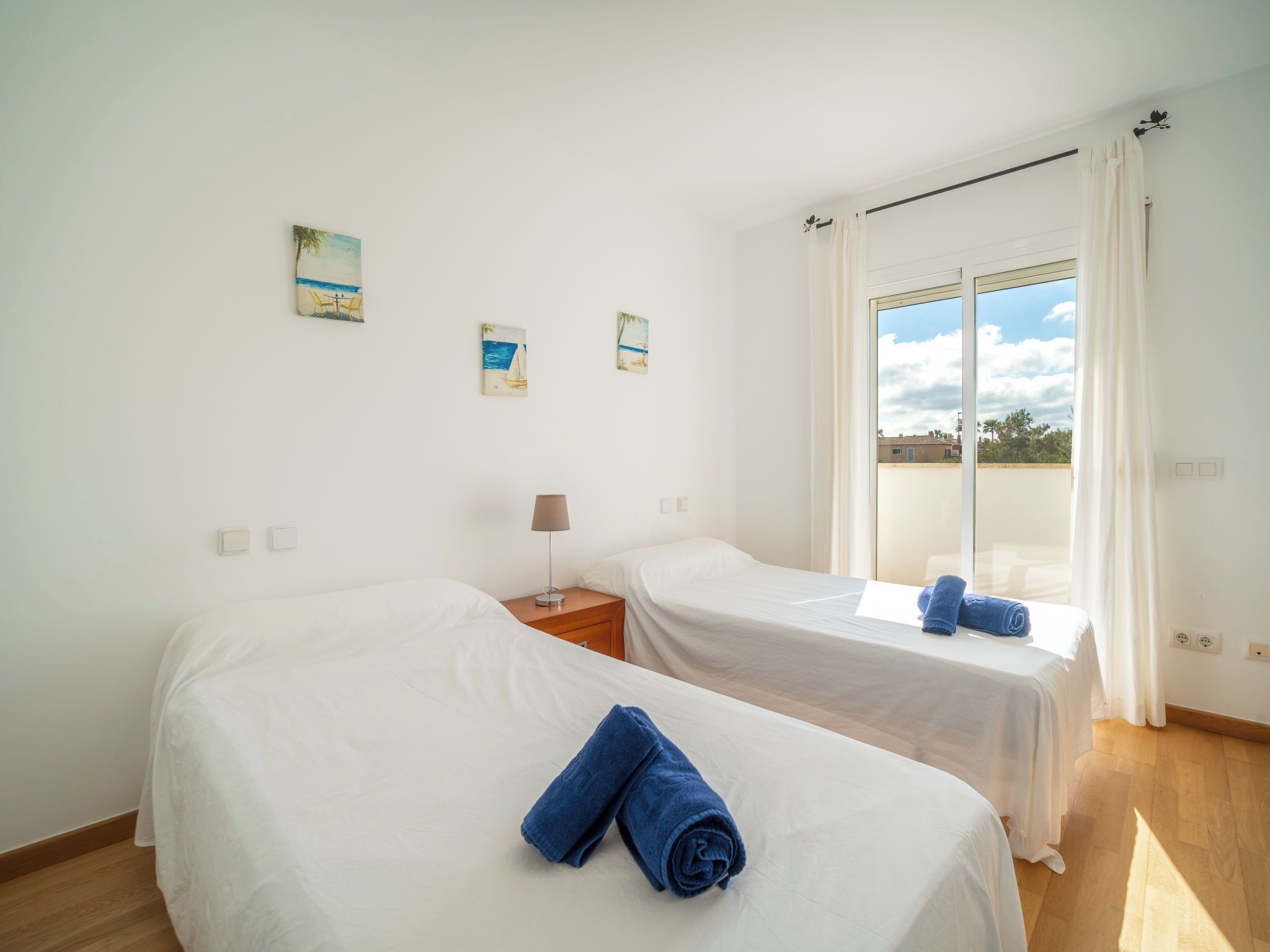 A hotel room with two beds, a window with curtains, and artwork on the walls.