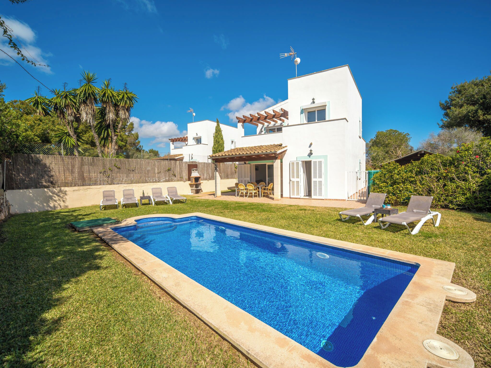 A swimming pool with lounge chairs, a patio area, and a white building with a tiled roof.