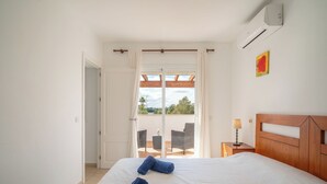 A bedroom with a bed, two rolled towels, a nightstand, a lamp, and a view of an outdoor balcony. - Son Ganxo I by Interhome (Cala Murada)