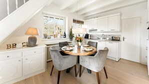 A dining area with a round wooden table, grey upholstered chairs, and a white cabinet with drawers. - House Harvestehude apartment "Küstenglück" (Sylt)