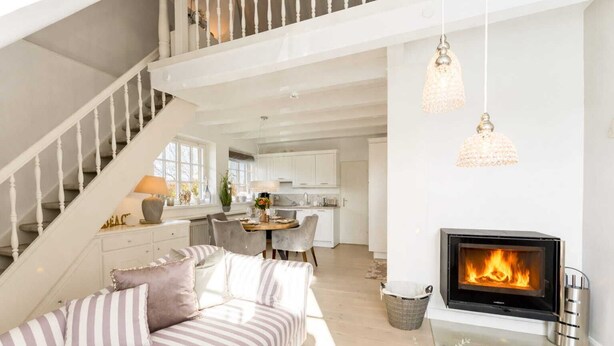 A modern living room with a fireplace, a staircase, and a dining area. - House Harvestehude apartment "Küstenglück" (Sylt)