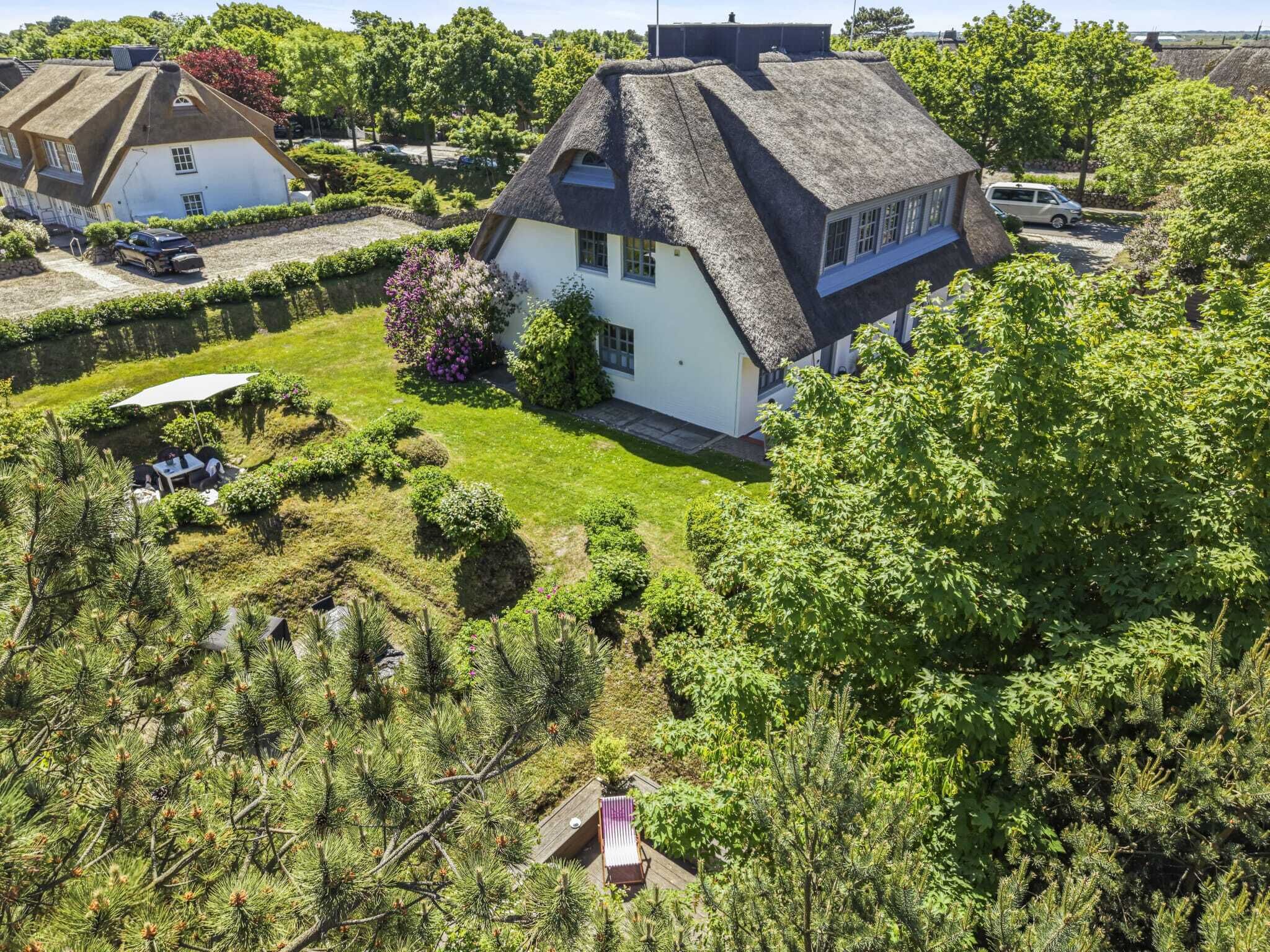 Une maison au toit de chaume, entourée d’un jardin bien entretenu et d’arbres.