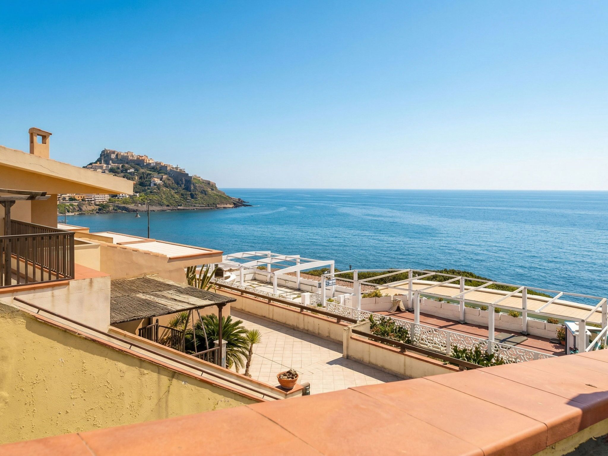 A terrace with a view of the sea and a hill with buildings.