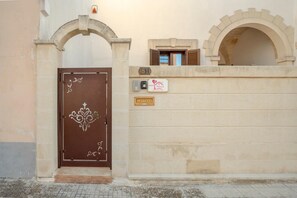 Una puerta marrón con un emblema decorativo, un buzón, un ventanal pequeño y una placa en una pared color beige.