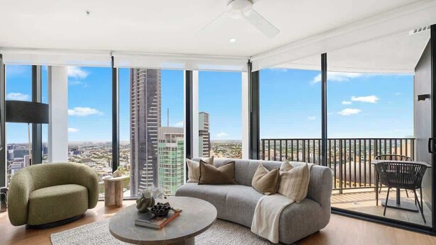 A modern living room with a sofa, armchair, and coffee table, large windows with a city view, and a balcony with a railing. - The Story Suite! 2Bed/2Bath/2Car/Pool/VIEWS ~ CBD (Brisbane City)