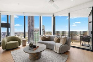 A modern living room with a sofa, armchair, and coffee table, large windows with a city view, and a balcony with a railing. - The Story Suite! 2Bed/2Bath/2Car/Pool/VIEWS ~ CBD (Brisbane City)