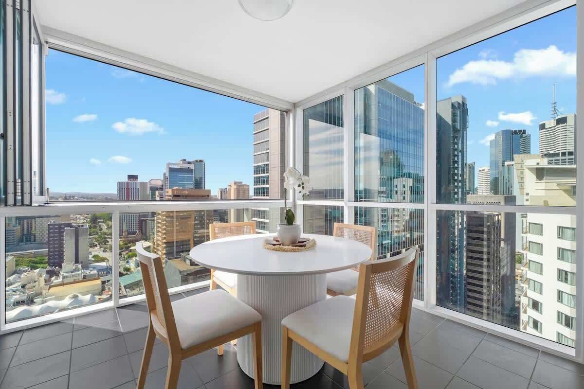 Une pièce moderne avec une table ronde et des chaises, de grandes fenêtres donnant sur la ville et un luminaire au plafond.