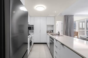 Une cuisine moderne avec des armoires blanches, des appareils en acier inoxydable et un grand îlot central doté d’un évier.