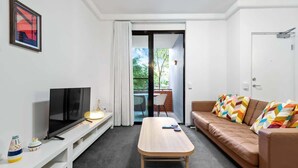 A modern living room with a TV, a wooden coffee table, a sofa with colorful cushions, and a sliding glass door leading to an outdoor area. - Trendy Teneriffe! ~ 1Bed, 1Bath, 1Car, Balconies (Teneriffe)