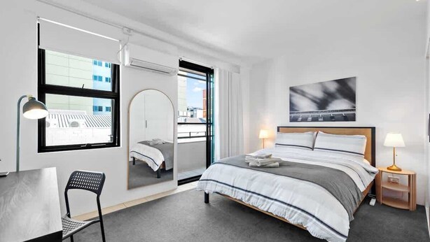 A modern hotel room with a bed, desk, chair, and large windows. - Trendy Teneriffe! ~ 1Bed, 1Bath, 1Car, Balconies (Teneriffe)