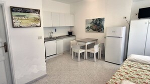 Una cuina compacta amb armaris blancs, una taula de dinar amb caires, un refrigerador i dos quadres penjats a la paret.