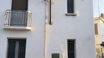 Een gebouw met een witte gevel, meerdere ramen met metalen tralies, een balkon met een metalen leuning en een stenen fundering.