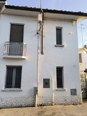 A building with a white facade, multiple windows with metal bars, a balcony with a metal railing, and a stone base. - DOLCECASA ENGRAVED (Sannazzaro de' Burgondi)