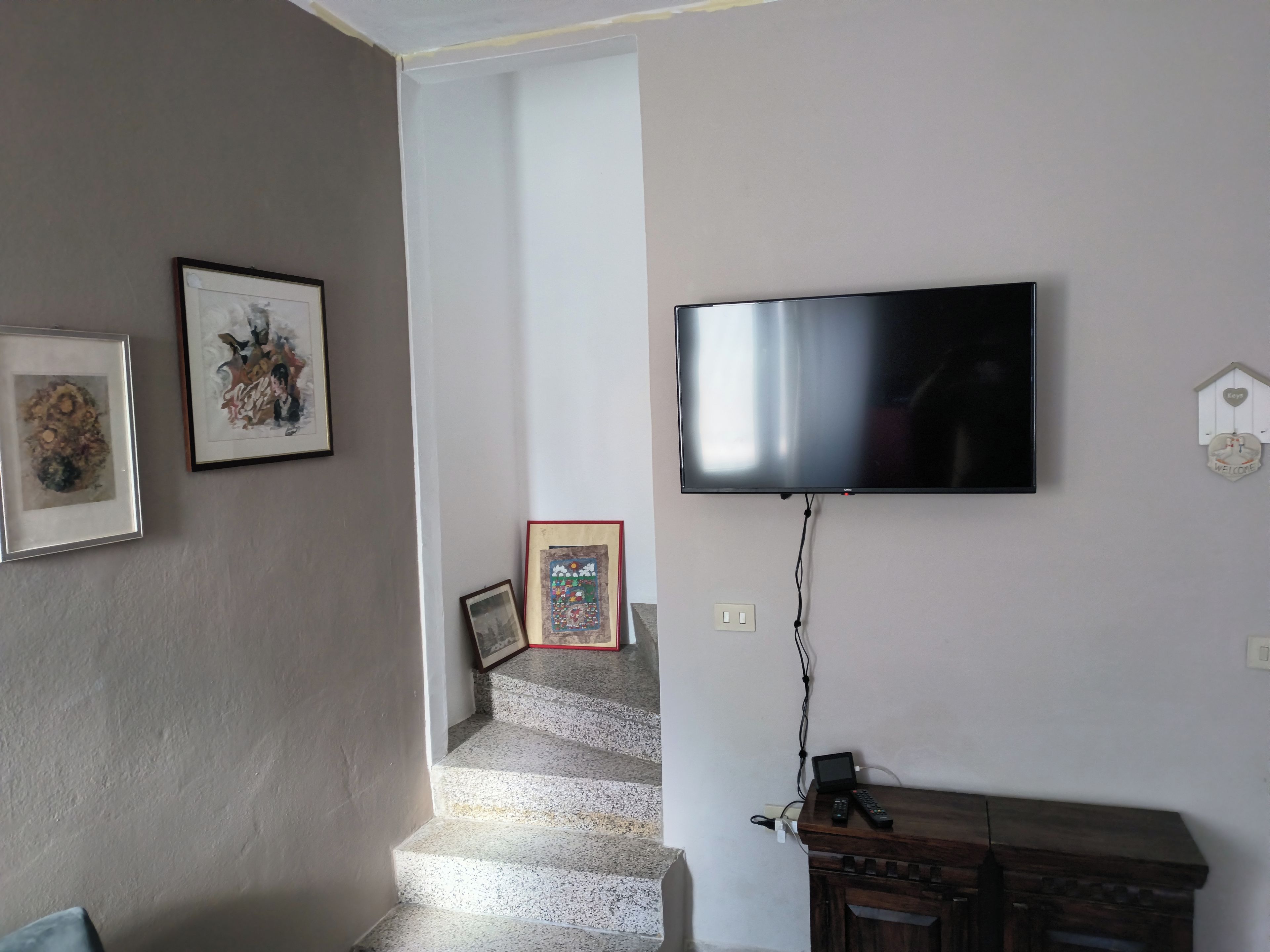 Sala de estar com televisão de tela plana na parede, escada que leva a outro nível e um armário de madeira.