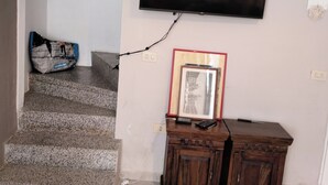 Ein Wohnzimmer mit einem flachbildfernseher an der Wand, einer Holzkommode und einer Treppe zu einem anderen Raum.