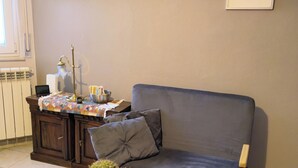 Ein Wohnzimmer mit einer Couch, einem Couchtisch mit Pflanze, einem Heizkörper und gerahmten Bildern an der Wand.