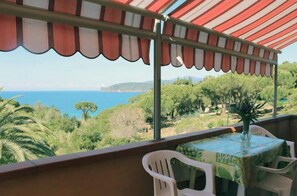 Ein Balkon mit Tisch und Stühlen, der auf eine Küstenlandschaft mit Bäumen und dem Meer blickt.