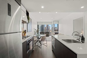 A modern kitchen with a central island, a dining area with chairs, a large window with a city view, and a built-in sink. - Fab! Skyline CBD views over South Bank! (South Brisbane)