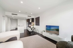 A modern living room with a flat-screen TV, a dining area, and a kitchen in the background. - Fab! Skyline CBD views over South Bank! (South Brisbane)