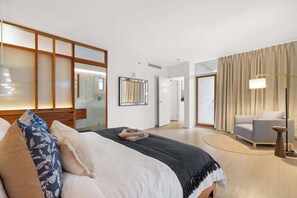 Ein Hotelzimmer mit einem großen Bett, einem Nachttisch, einem Sessel, einem Spiegel und einer Lampe.