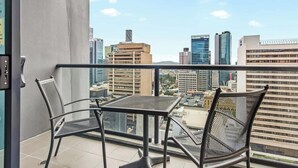 Ein Balkon mit zwei Stühlen und einem Tisch, der Blick auf die Stadt bietet.
