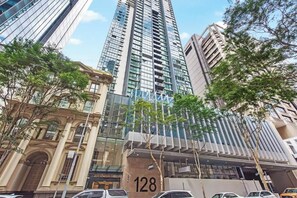 A high-rise building with a modern glass facade, a classical building with arched windows, and a tree-lined street. - City Centre! 1Bed/1Bath/Study/1Car/Balcony ~ CBD (Brisbane City)