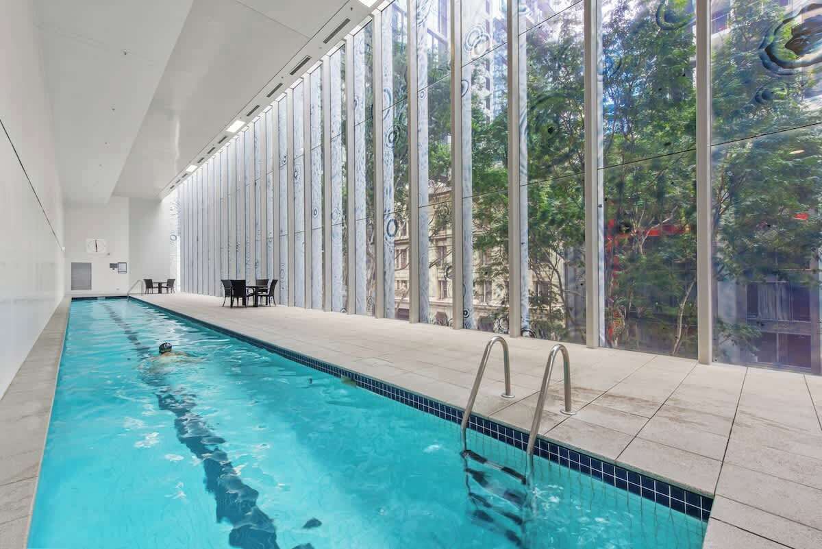 Ein überdachter Schwimmbereich mit großen Glaswänden, Fliesenboden und Blick auf Grünflächen.