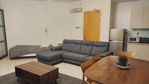 En moderne stue med en grå hjørnesofa, et træ sofabord og et spisebord med stole. En lille potteplante står på spisebordet.
