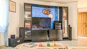 Un salon avec une table basse en verre, un téléviseur, une bibliothèque et un élément décoratif mural.