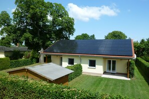 A house with a solar panel roof, a small deck, and a well-maintained garden. - Vacation apartment Haus Vietzen 1 with garden and terrace in Rechlin, also for dogs (Rechlin)