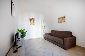 Ein Wohnzimmer mit einem braunen Sofa, weißen Regalen und zwei gerahmten Bildern an den Wänden.