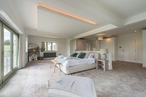 Une chambre spacieuse avec un grand lit, des tables de chevet, un banc et une vue sur l’extérieur.