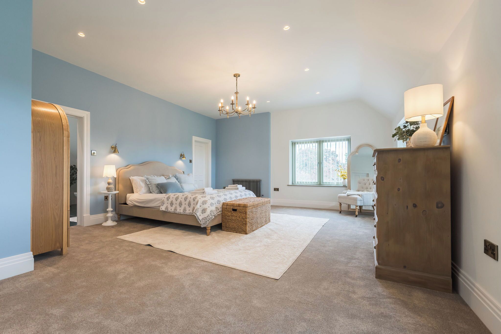 A bedroom with a bed, bedside tables, a chandelier, a dresser, and a window.