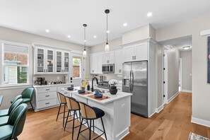 Une cuisine moderne avec des meubles blancs, des appareils en acier inoxydable et un îlot central doté de tabourets de bar.