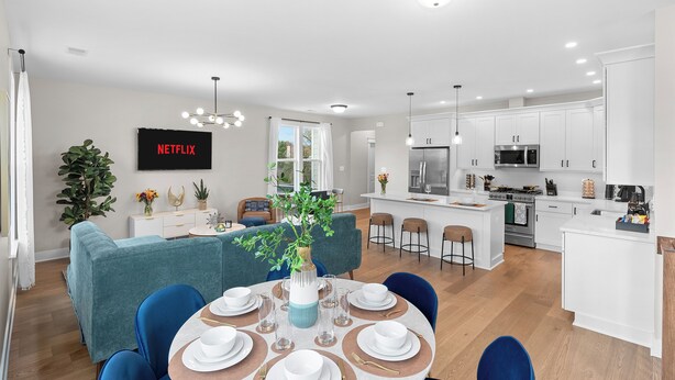 Cocina moderna con armarios blancos, una isla central y una zona de comedor con sofá azul y mesa redonda.