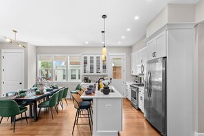Une cuisine moderne dotée d’un îlot central, d’appareils électroménagers en acier inoxydable et d’un coin repas avec des chaises vertes.