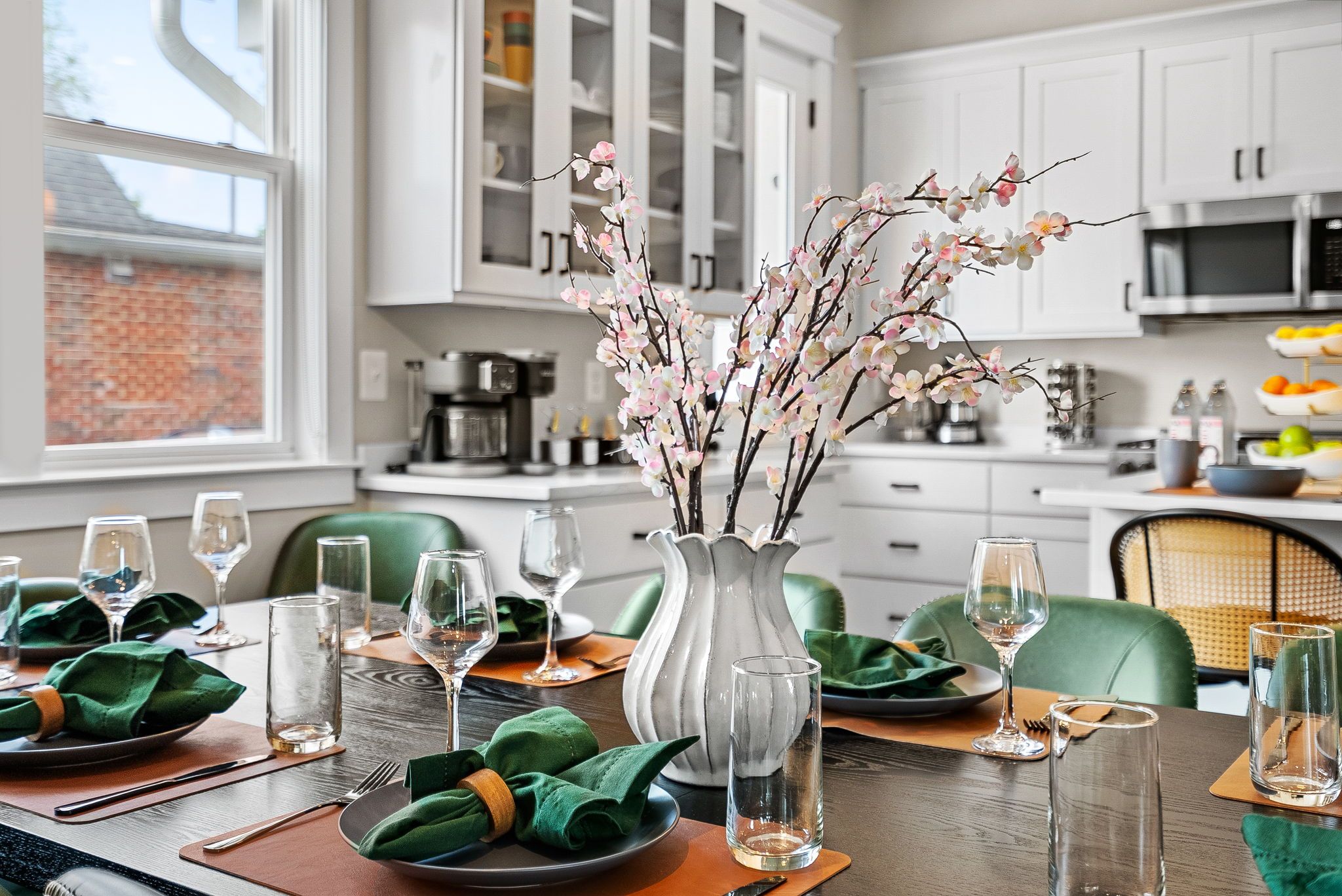 A dining table set with green napkins, wine glasses, and a vase with branches.