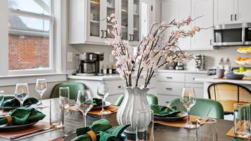 A dining table set with green napkins, wine glasses, and a vase with branches.