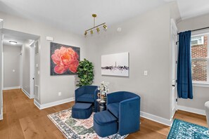 Un salon moderne agrémenté d’un grand tableau floral, d’une œuvre d’art représentant un paysage urbain et d’un canapé bleu.