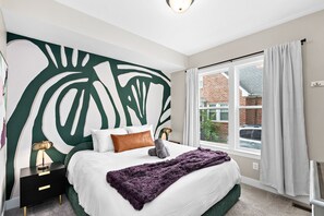 Ein Schlafzimmer mit einem großen Bett, einer Wandmalerei, einem Fenster mit Vorhängen und einem Nachttisch mit Lampe.