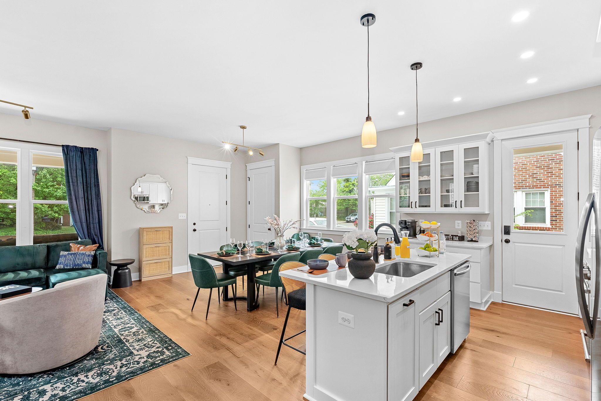 A modern kitchen with white cabinetry, a central island, and a dining area with green chairs.