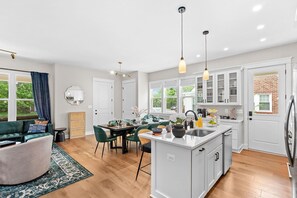 Une cuisine moderne avec des meubles blancs, un îlot central et un coin repas agrémenté de chaises vertes.