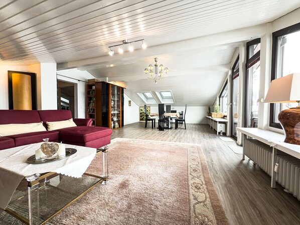 Un loft spacieux avec un plafond haut, un canapé rouge, un coin repas et des fenêtres de toit.