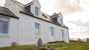A white building with a gabled roof, a stone wall, and a wheelbarrow. - Ben Edra Croft by Interhome (North Skye)